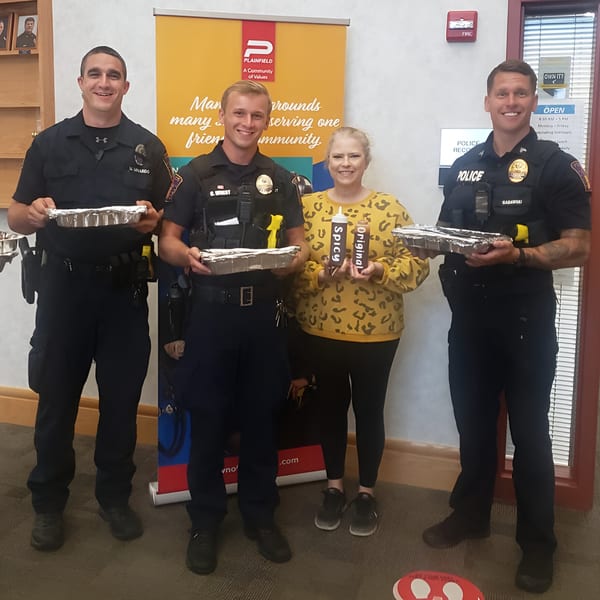 Three police officers and a woman hold foil pans of Double D's Southern BBQ and sauce bottles.