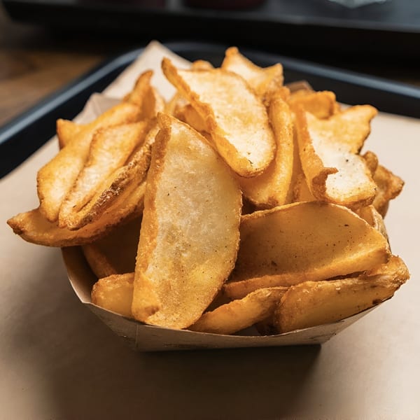 A paper boat filled with golden-brown, seasoned potato wedge fries on a light brown surface.