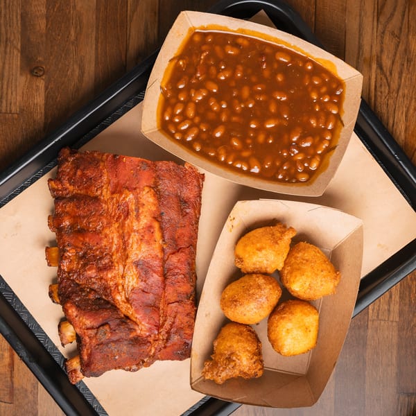Double D's Southern BBQ ribs, baked beans, and hush puppies on a black tray.