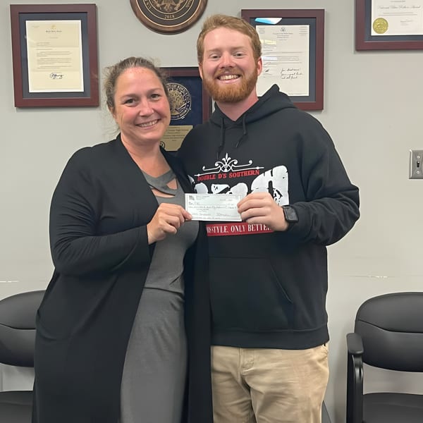 A man in a Double D's Southern BBQ hoodie and a woman hold up a check.