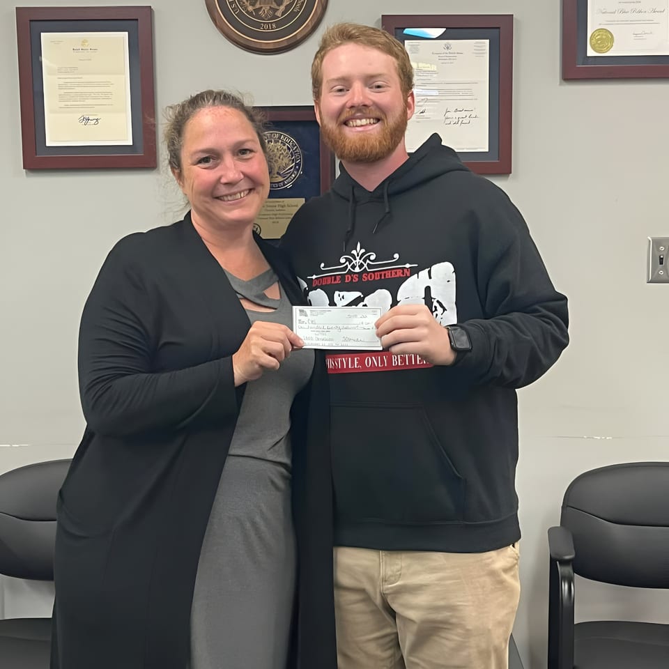 A man in a Double D's Southern BBQ hoodie and a woman hold up a check.