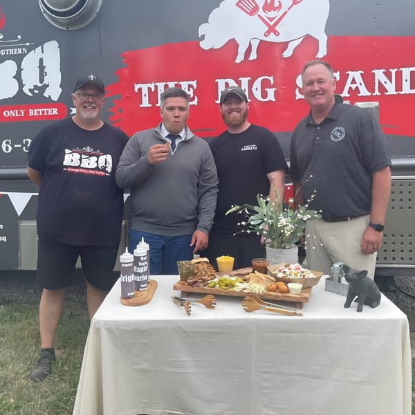Four men stand by a Double D's Southern BBQ food truck with a table of BBQ dishes.