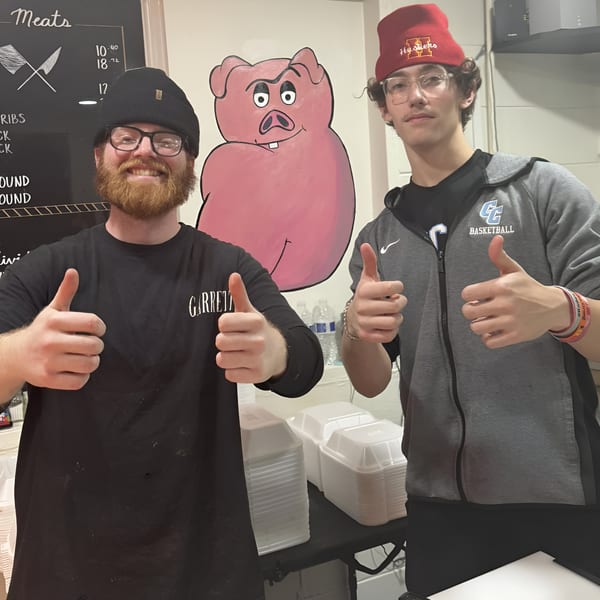 Two smiling men giving thumbs up in front of a Double D's Southern BBQ pig mural.