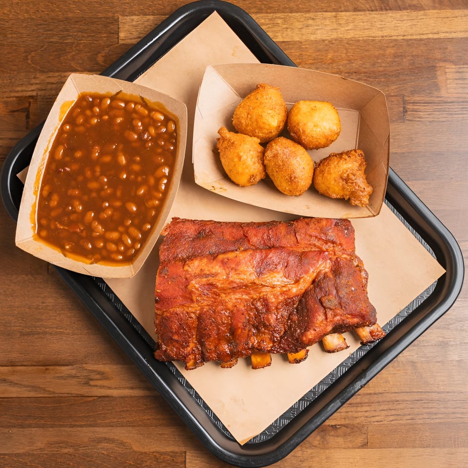 Double D's Southern BBQ ribs, baked beans, and hush puppies on a black tray.
