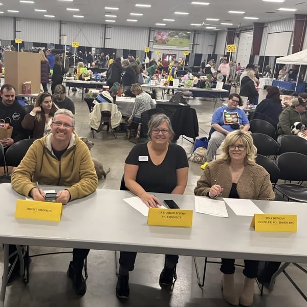 Three people, including Tina Duncan from Double D's Southern BBQ, seated at a table in a large event hall.