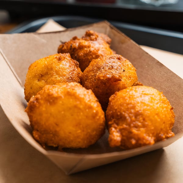 Five golden-brown hush puppies from Double D's Southern BBQ in a rustic paper tray.